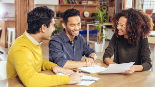 Une femme et deux hommes discutent autour d'une table.