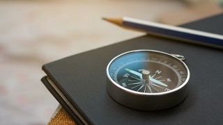 A compass and a pencil are on the black notebook.