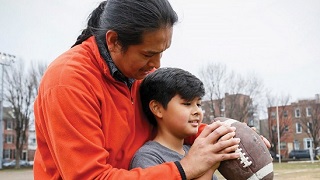 A man is instructing how to hold a football to a boy.