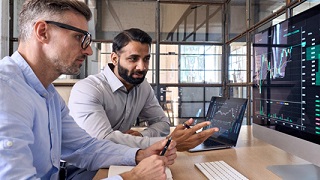 Two men are looking at a chart on the monitor.